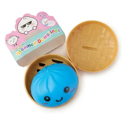 A cute blue steamed dumpling toy with a smiling face, presented inside a round beige basket-style container next to its pink and blue packaging box.