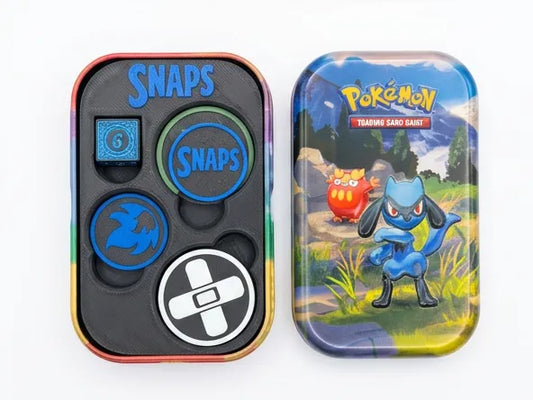 Pokémon Teaching Sand Shaker set shown with its rainbow-edged metal tin, featuring four game pieces inside and the illustrated tin beside it on a white background.